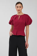 Woman wearing a red blouse with puff sleeves on a plain background